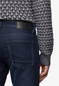 Jeans blu scuro abbinati a un maglione in maglia testurizzata di colore blu navy e grigio chiaro. I jeans presentano un'etichetta in pelle nera sulla vita.
