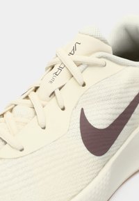 Zbliżenie beżowych butów do biegania Nike Vaporfly Lite z beżowym sznurowadłem i ciemnobrązowym logo Nike swoosh na siateczkowej tkaninie.