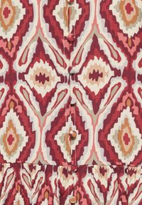 Tissu avec motif géométrique en losanges rouge, rose, beige et blanc, avec des boutons recouverts de tissu au centre.