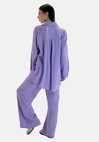 Conjunto de dos piezas de color lavanda hecho de tela texturizada, que presenta una camiseta de ajuste holgado con cuello y pantalones acampanados.