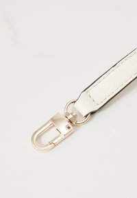 Witte leren band met een gouden metalen sluiting en accent. Soepele textuur met contrasterende donkere randelementen. Compact ontwerp.