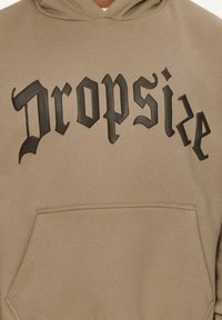 Kaki Kapuzenpullover mit einer Fronttasche, versehen mit schwarzen erhabenen Text, der "Dropsize" in einer dekorativen Schriftart liest. Glattes Material, lässiges Design.
