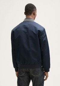 Chaqueta bomber de color marino con textura suave, puños y cuello acanalados con franjas blancas; diseño ajustado con cintura elástica.