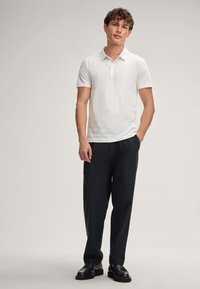 Witte getextureerde polo met een kraag, gecombineerd met donkere broeken en zwarte schoenen. Eenvoudig ontwerp, korte mouwen, strakke lijnen.