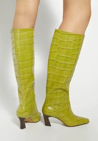 Green faux crocodile leather knee-high boots with pointed toe and tapered heel, featuring a zip closure on the side for easy wear.