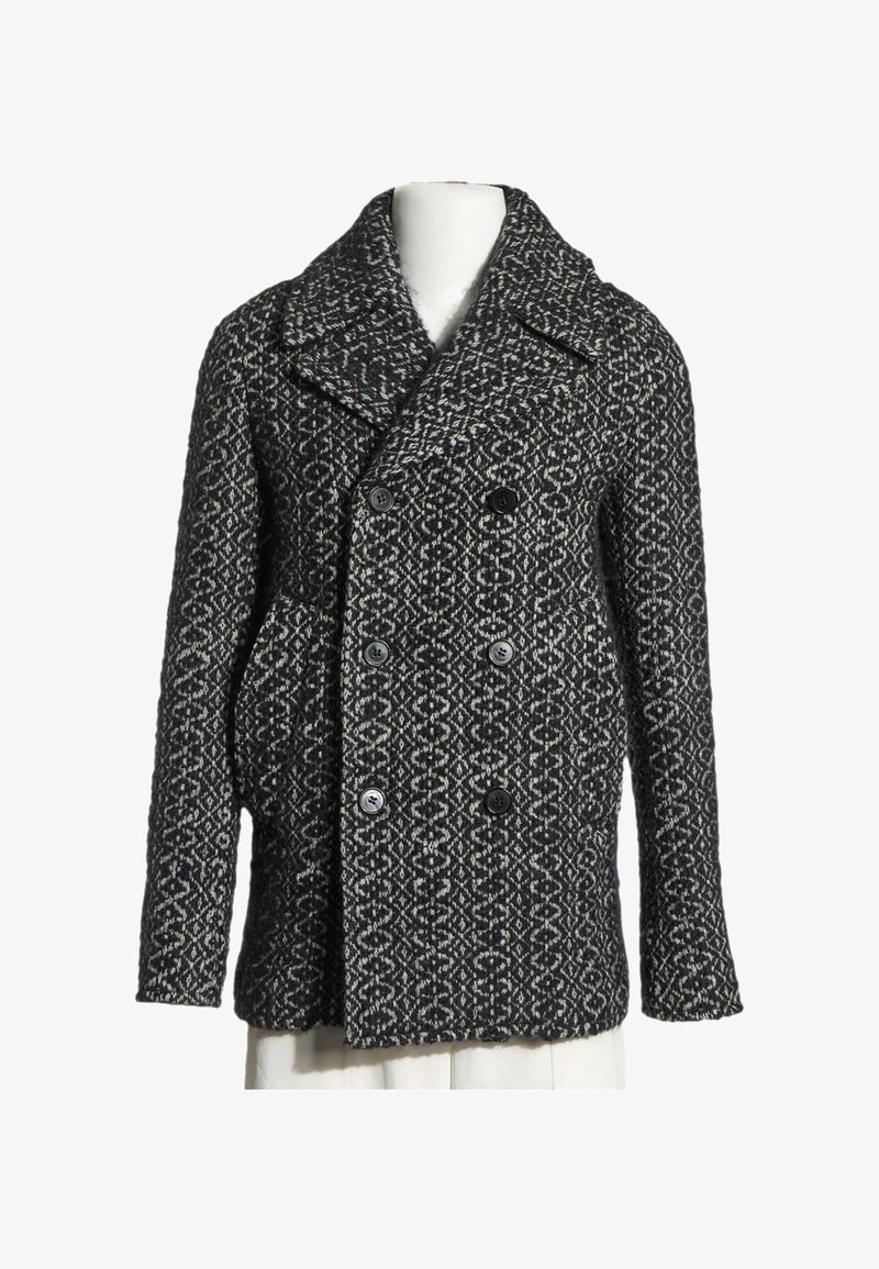 Manteau en laine à motifs noirs et blancs, croisé, avec de larges revers et six boutons, exposé sur un buste de mannequin blanc.
