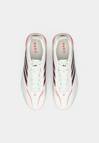 Λευκά ποδοσφαιρικά παπούτσια με μαύρες ρίγες και κόκκινες λεπτομέρειες. Λείο συνθετικό υλικό, στρογγυλεμένη μύτη, κορδόνια και επενδεδυμένο εσωτερικό.