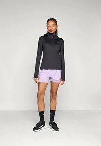 Svart långärmad topp med dragkedja i kragen, kombinerad med ljuslila shorts. Svarta sportstrumpor och skor fulländar outfiten.