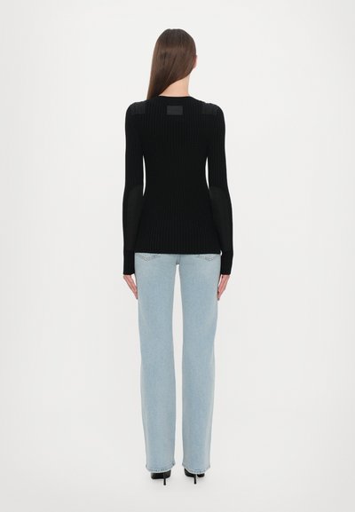 Black ribbed sweater with long sleeves, featuring leather shoulder accents. Paired with light blue wide-leg jeans and black heeled shoes.