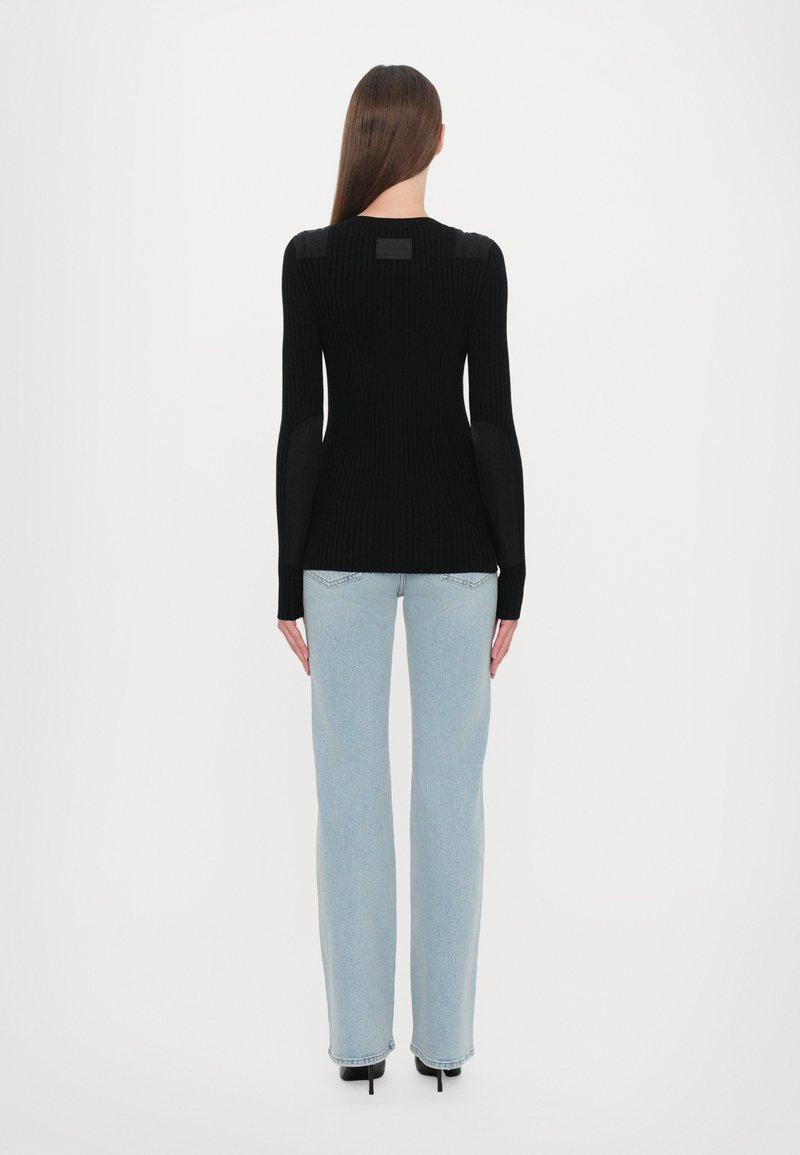 Pull noir à côtes avec des manches longues, présentant des accents d'épaule en cuir. Associé à un jean large bleu clair et des chaussures à talons noires.