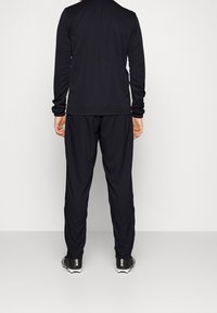 Černý sportovní top s dlouhým rukávem a odpovídající kalhoty, vyrobené z hladké, prodyšné látky. Má volný střih a elastický pas.