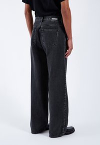 Široké černé dž�íny z denimu s opraným vzhledem, s pěti kapsami a logem na pásku. Textil vypadá odolně a texturovaně.
