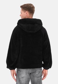 Czarna bluza polarowa z dużym kapturem, ściągaczami na rękawach i luźnym krojem. Miękka w dotyku, bez widocznych logo czy wzorów.