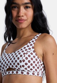 Floral-patterned bikini top in white and brown. Features a scoop neckline and a cut-out detail under the bust. Made from stretchy fabric.