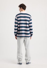 Pitkähihaine pusero tummansinisen, vaaleanpunaisen ja vihreän raidallisen kuosin kanssa. Suunniteltu valkoisella kauluksella ja ribbausvarrella, yhdistettynä harmaisiin collegehousuihin.