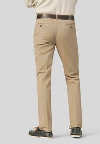 Beige Chinos aus Baumwolle mit slim fit, ausgestattet mit Gesäßtaschen und einem braunen Gürtel. Kombiniert mit dunklen Schuhen, die ein schlichtes Design zeigen.