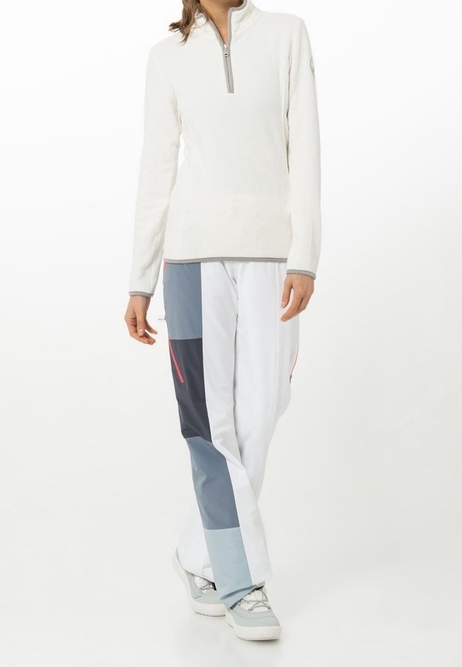 Persona vestida con un pulóver blanco de cremallera hasta el cuarto y pantalones en bloques de color en blanco, gris y azul marino, con zapatillas de colores claros.