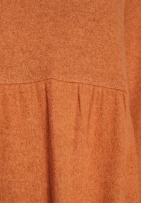 Tejido de color óxido, con una textura suave y un detalle de costura fruncida. El material parece ligeramente difuso y tiene una apariencia uniforme.