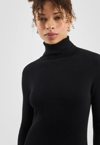 Schwarzer gerippter Rollkragenpullover mit figurbetontem Schnitt und langen Ärmeln, gefertigt aus einem weichen Strickmaterial.