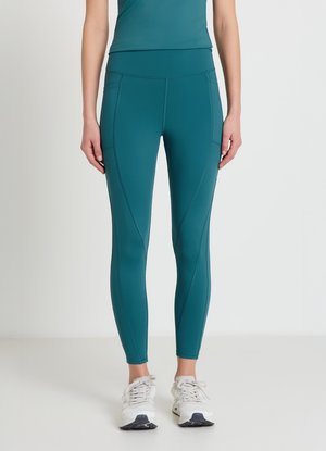 Türkisfarbene Workout-Leggings mit hohem Bund, aus glattem Stoff, mit Seitennähten und figurbetontem Schnitt. Kombiniert mit hellgrauen Sportschuhen.