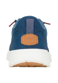 Sneaker blu scamosciato con suola bianca, dotata di una toppa in pelle marrone con la scritta "HEY DUDE" e un tassello sul tallone testurizzato con accenti rossi.