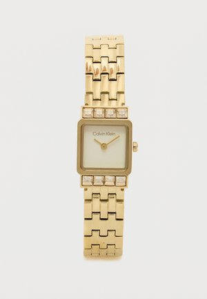 Zlatni kvadratni ručni sat s metalnom narukvicom, s bijelim brojčanikom i malim kristalnim naglascima na okviru. Brand: Calvin Klein.