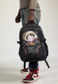 Mochila negra con gráfico de personaje de dibujos animados, detalle de sombrero de paja, acentos naranjas, múltiples compartimentos, correas acolchadas y bolsillos laterales de malla.