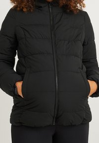 Chaqueta acolchada negra con cierre frontal de cremallera, diseño acolchado y puños elásticos, que cuenta con bolsillos laterales y un cuello subido.