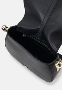 Sac bandoulière en cuir noir avec quincaillerie dorée, rabat ouvert montrant l’intérieur avec une poche zippée et une fermeture à bouton magnétique.