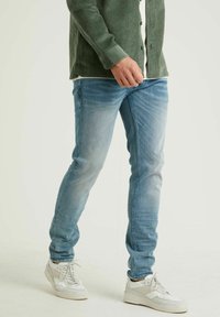 Vaqueros de mezclilla azul claro con corte ajustado, que presentan un ligero desgarro y un acabado ligeramente desvaído. Combinados con zapatillas blancas.
