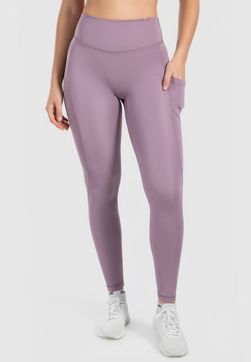 Leggings lilas avec une taille haute, tissu texturé et poche latérale. Présente un design élégant et ajusté associé à des chaussures de sport blanches.