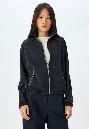 Black zip-up jacket with a high collar, elastic waistband, and side pockets. Features smooth texture and subtle sheen.