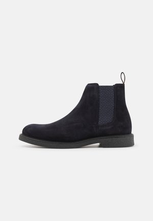 Maine nubuck Chelsea-kengät, joissa on teksturoitu elastinen paneeli, pyöreä kärki ja musta teksturoitu kumipohja. Takana vetolenksu helppoa pukemista varten.