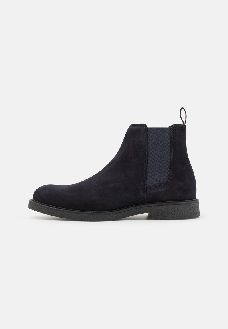 Bottines Chelsea en suede bleu marine avec un panneau élastique texturé, bout rond et une semelle en caoutchouc texturé noir. Tirette à l'arrière pour un enfilage facile.