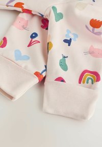Jasnoróżowa dziecięca bluza z multikolorowymi abstrakcyjnymi wzorami, w tym twarzami kotów, sercami i kwiatami. Żebrowane mankiety w dopasowanej tkaninie.