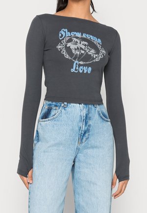 Mørkegrå langærmet trøje med bådhals, prydet med blå blomstermotiv og teksten "Show some Love" i midten, parret med lyseblå jeans.