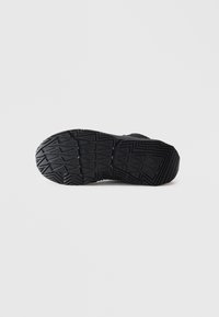 Semelle de chaussure de sport noire avec des motifs de semelle géométriques présentée sur un fond blanc.