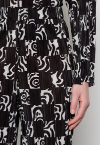 Czarnobiała tkanina w wzory z abstrakcyjnymi spiralami o prążkowanej strukturze, z dopasowanym pasem i długimi rękawami.