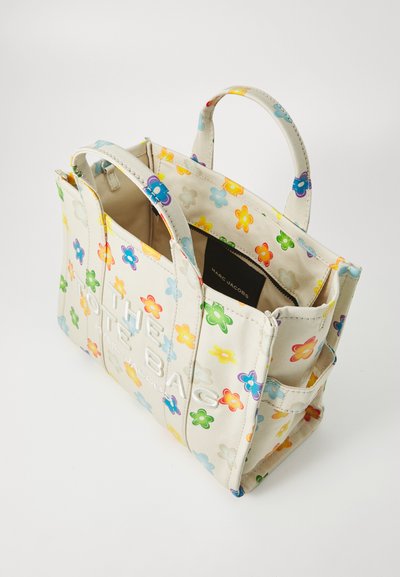 Lærret tote-veske med fargerik blomstermønster; har doble håndtak på toppen og preget tekst; innvendig lomme synlig; kremfarget bakgrunn.