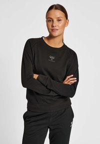 Svart sweatshirt med rund hals och långa raglanärmar. Har en subtil logotyp på bröstet och ribbade fållar för en åtsittande passform.