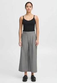 Zwarte aansluitende tanktop gecombineerd met hoogsluitende, wijde grijze broek en robuuste zwarte schoenen met studaccenten.