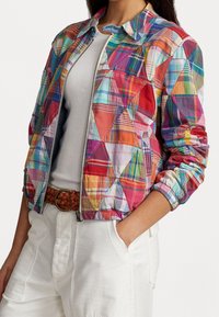 Wielokolorowa kurtka w kratę z zamkiem z przodu, elastycznymi mankietami i skróconym krojem. Zawiera aplikacje z różnymi fakturami i wzorami.