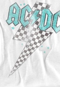 AC/DC-Logo in Blau mit einem leicht gestreiften Blitz und kleinen blauen Sternen auf einem weißen Stoffhintergrund.