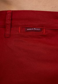 Pantaloni di cotone rossi con una texture liscia, cuciture in contrasto e un'etichetta con la scritta "CIPO & BAXX" vicino alla vita.