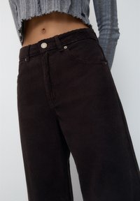 Bruine corduroy wijde broek met verticale ribbels, voorzien van een voorknop, ritssluiting en zijzakken. Gestyled met een cropped grijze top.