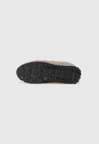 Suola di sneaker color tan caratterizzata da una suola in gomma nera testurizzata con un motivo di quadrati e rettangoli, che offre aderenza.