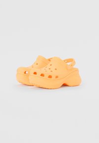 Sabots en plastique orange avec des trous de ventilation, une sangle au niveau du talon réglable et une semelle texturée pour une bonne adhérence. Design courbé avec une épaisse semelle.