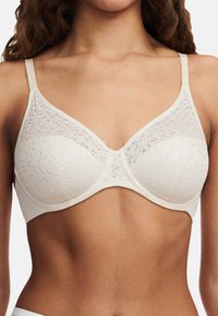 Weißer Spitzen-BH mit dreieckigen Cups aus glattem Stoff, verstellbaren Trägern und einem dezenten Blumenmuster auf der Spitze.