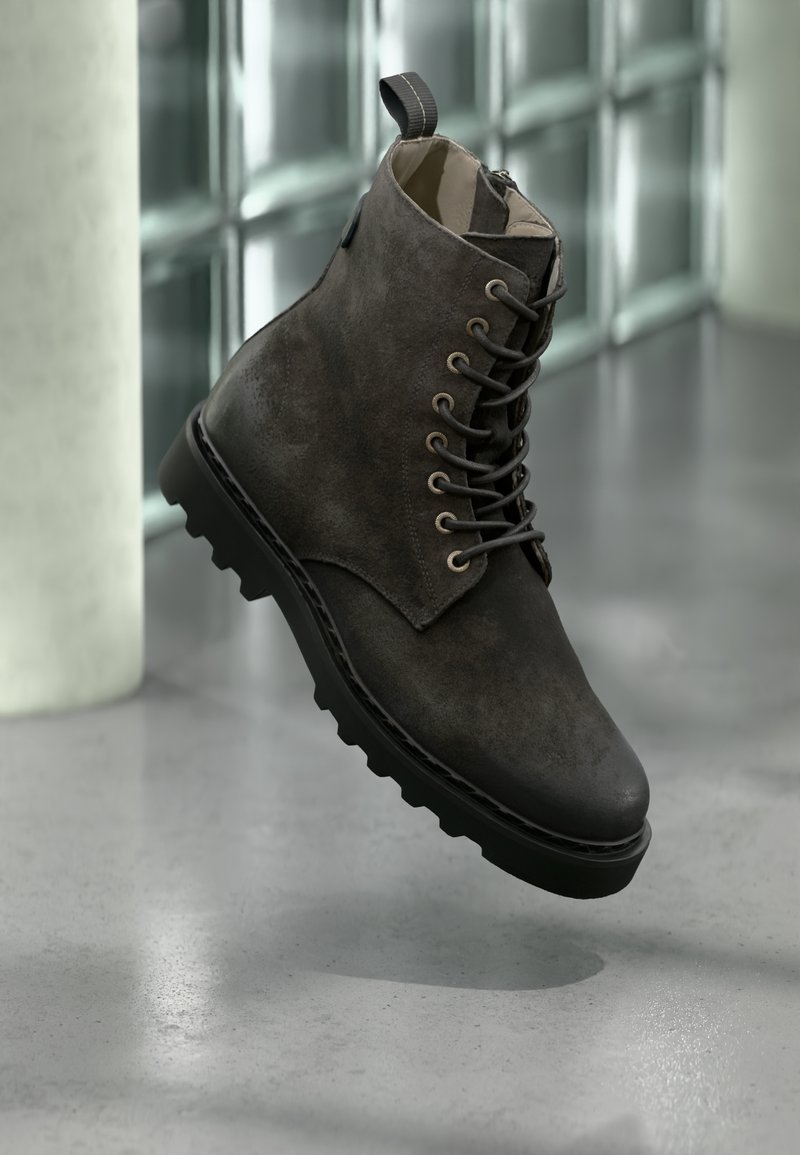 Bota corta de cuero gris oscuro con puntera redonda, ojales metálicos y superficie texturizada. Cuenta con una suela resistente con tracción y una presilla superior.