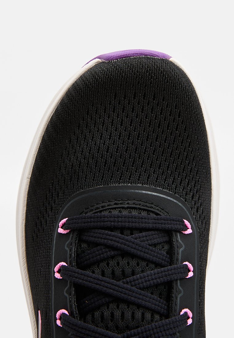 Zapatilla deportiva negra con una parte superior de malla transpirable, que presenta cordones negros con acentos rosas y una suela blanca. Diseño de puntera redondeada.